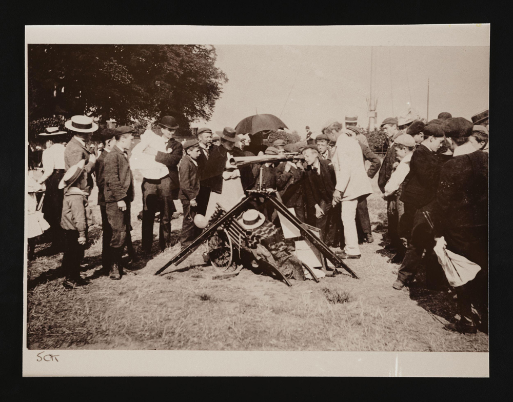 A photograph of a crowd gathering round a boy looking through a telescope. 