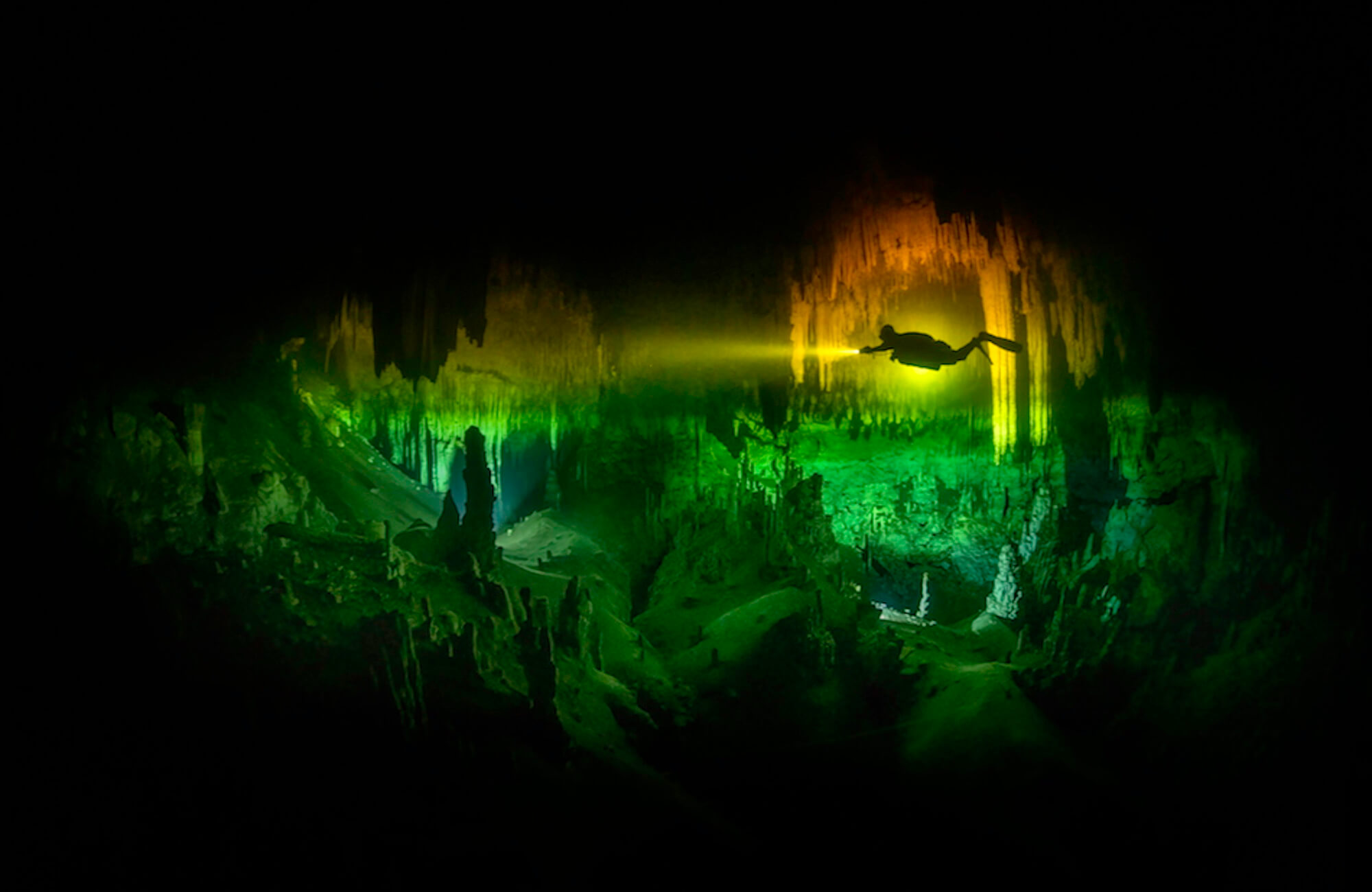 ‘Suspended In A Tannic Acid Rainbow, A Diver Explores The Deli Shop Chamber Of Cenote Chikin Ha’ By Martin Broen